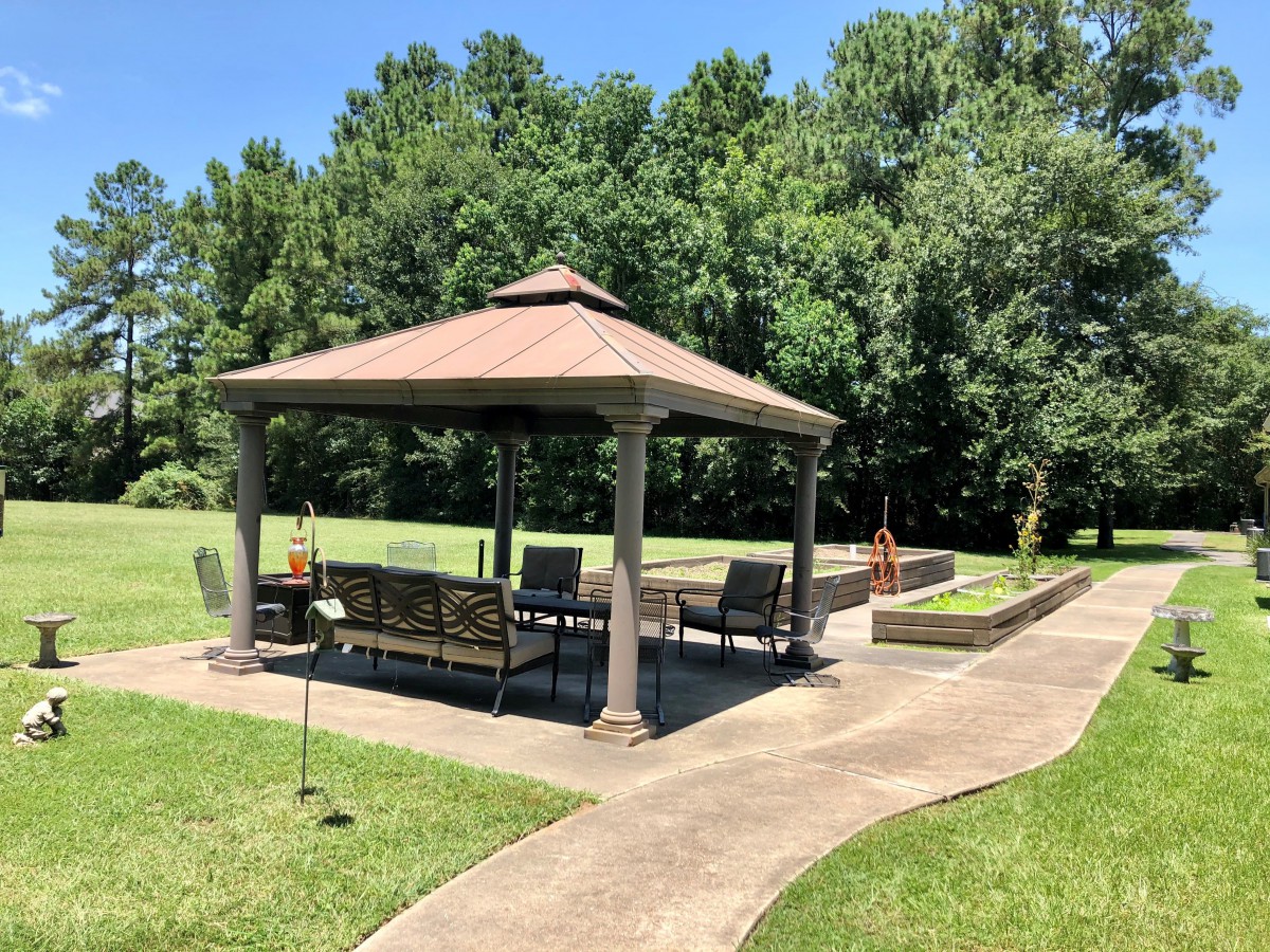 A relaxing outdoor gazebo with patio furniture, surrounded by a lush lawn and trees.