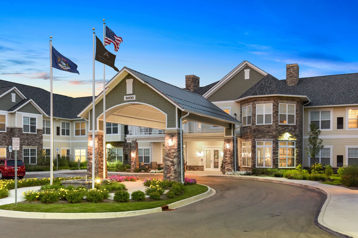 A well-lit building entrance with flags and landscaped surroundings during evening.