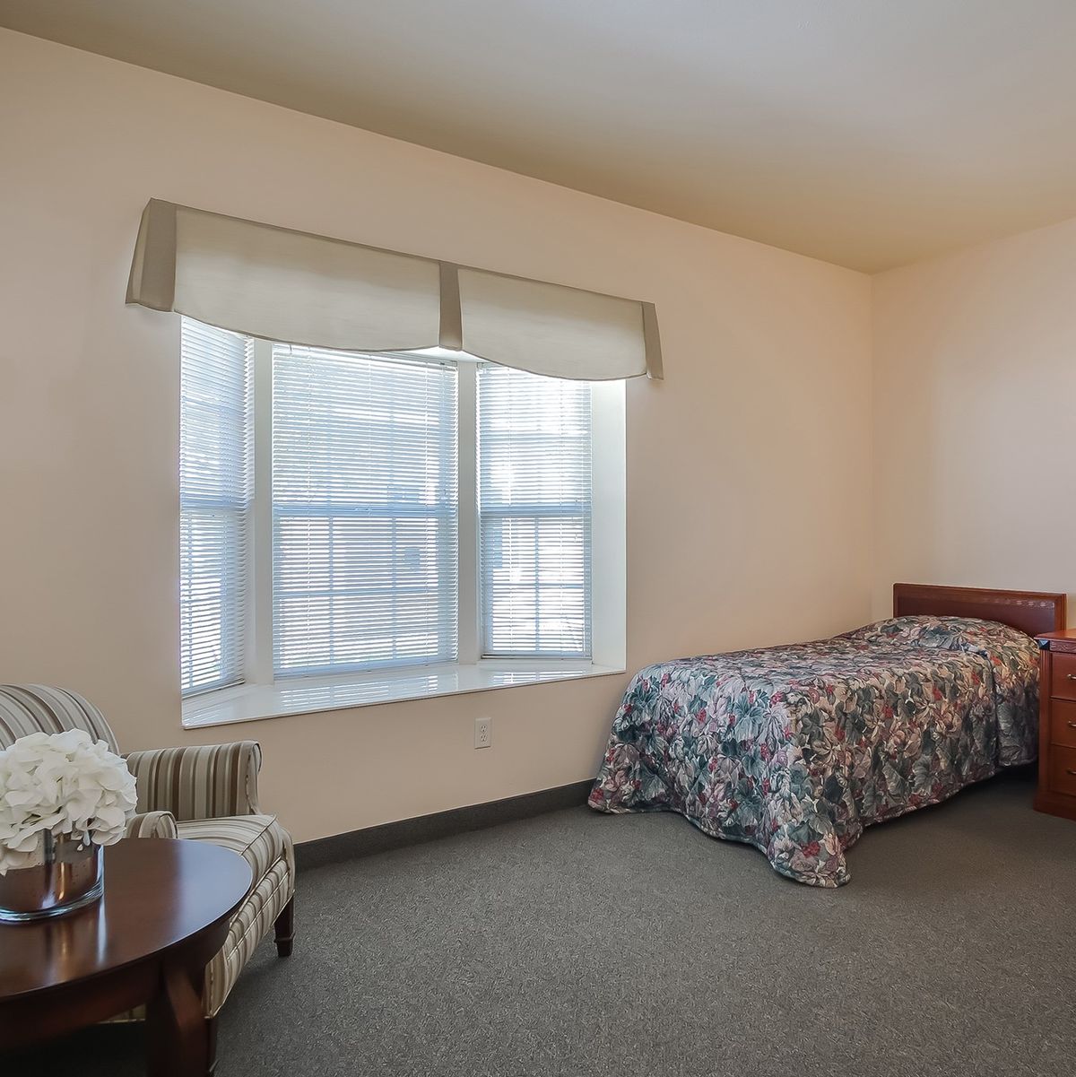 A minimalist bedroom with a single bed, window, and table with flowers.