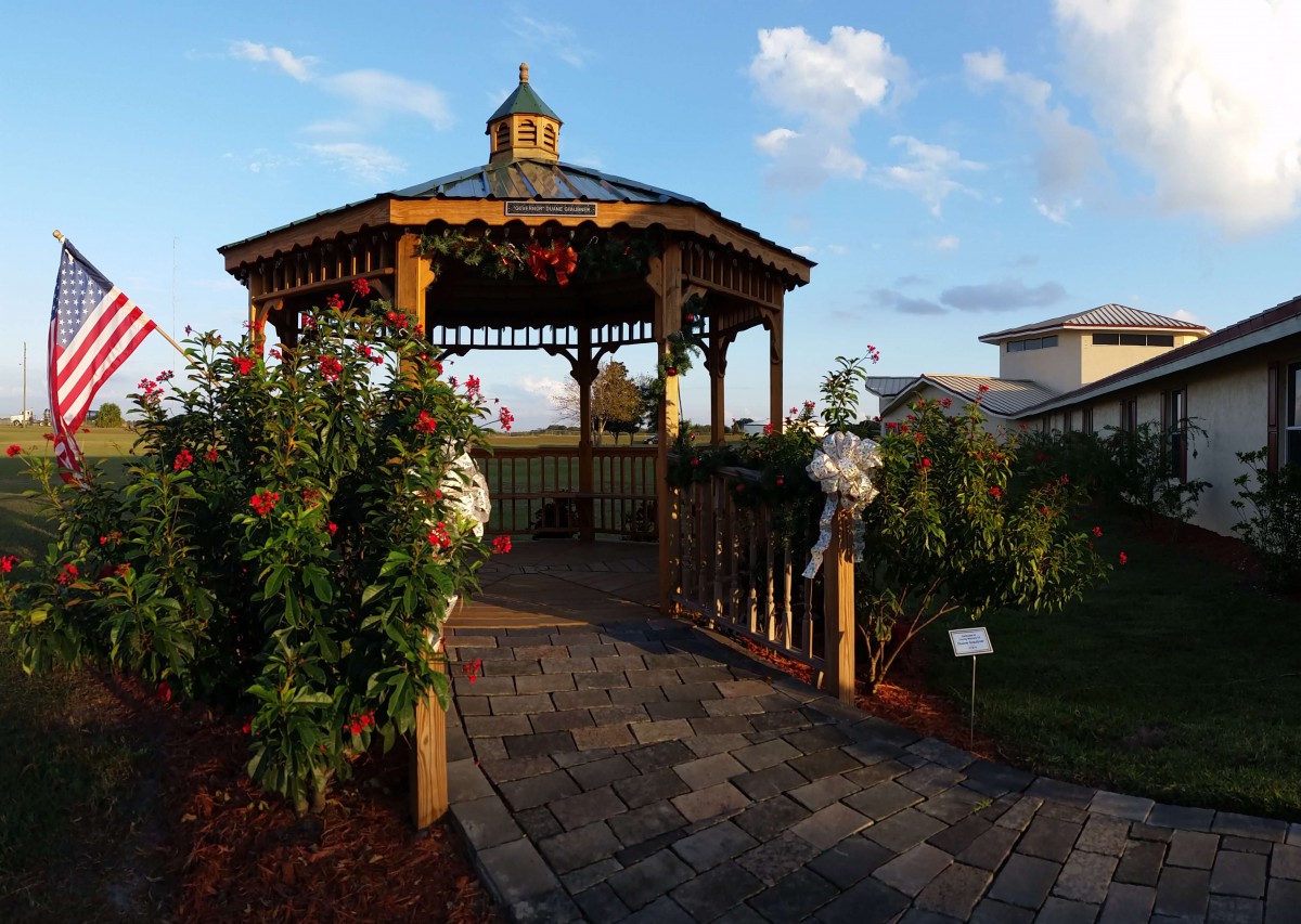 A charming wooden gazebo in a garden setting with blooming flowers and a small bridge.
