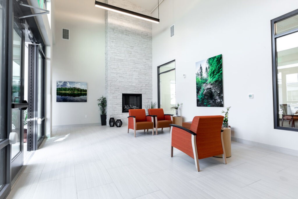 A modern, minimalist living room featuring white walls, a fireplace, and orange armchairs complemented by vibrant artwork.