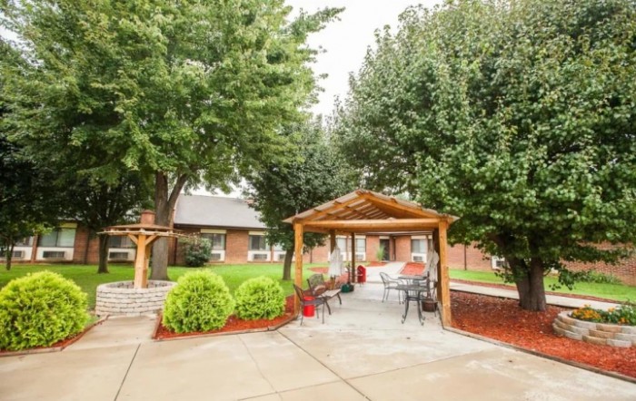 A cozy outdoor gazebo surrounded by trees and landscaping, featuring benches and a paved patio.