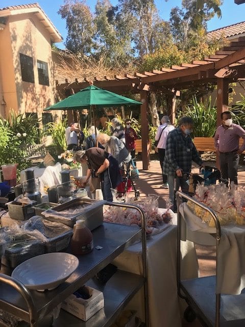 People browsing items at an outdoor market in a garden setting.