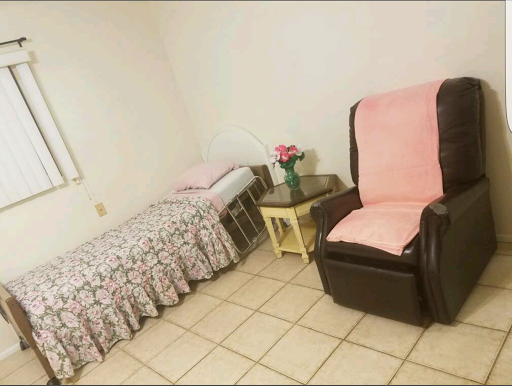 A cozy bedroom setup featuring a bed, a recliner chair, and a small table with flowers.