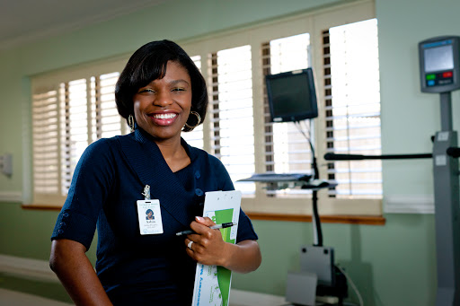 A healthcare professional smiling while holding a clipboard in a medical office.