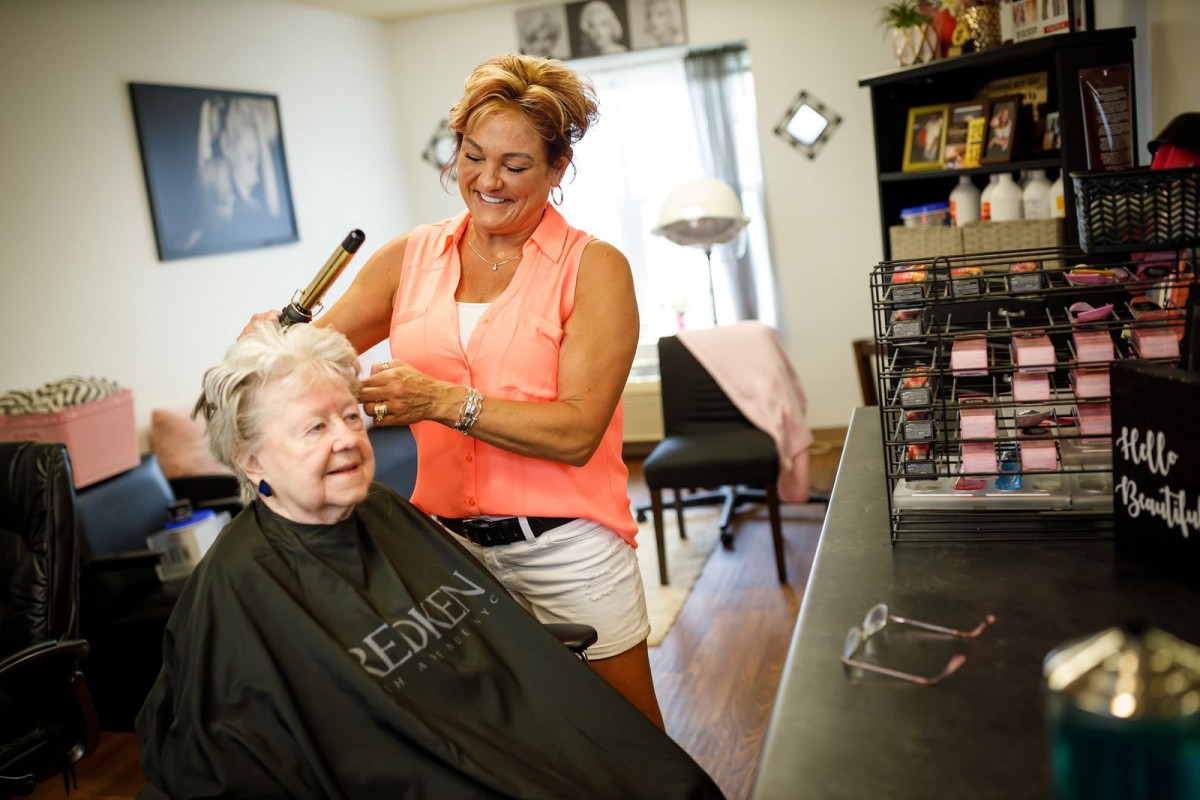 A hairdresser styling an elderly woman's hair in a salon.