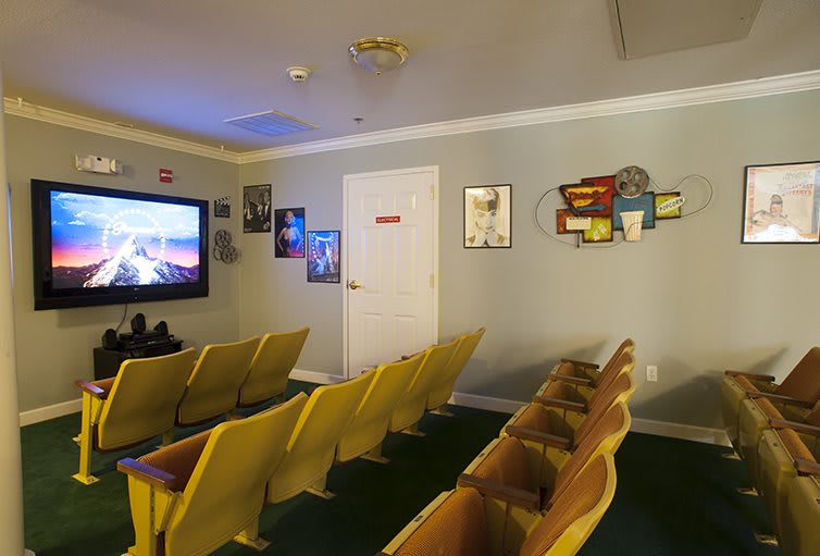 A small indoor theater room with rows of yellow chairs facing a large screen, adorned with movie posters on the walls.