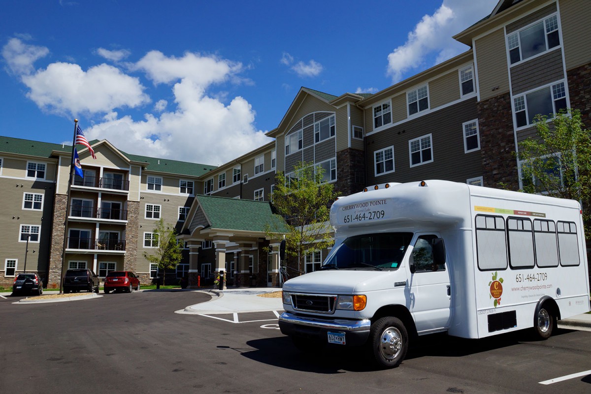 A shuttle van parked in front of a large apartment complex on a sunny day.