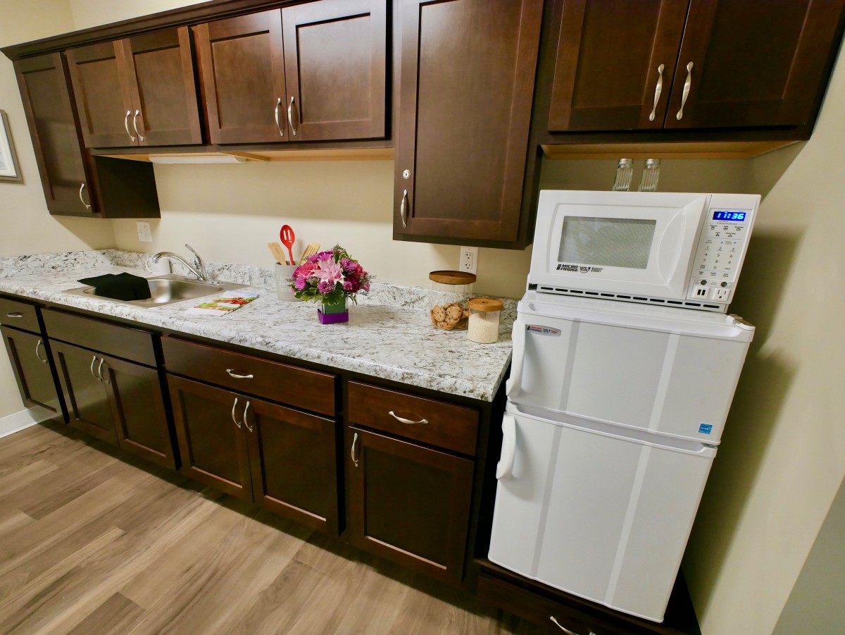 A cozy kitchen with dark wooden cabinets, a countertop adorned with flowers, and essential appliances like a microwave and refrigerator.