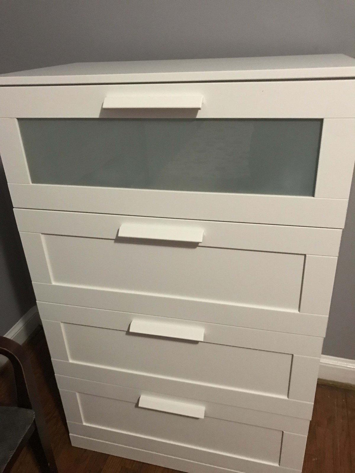 A white dresser with four drawers, featuring a frosted glass panel on the top drawer.