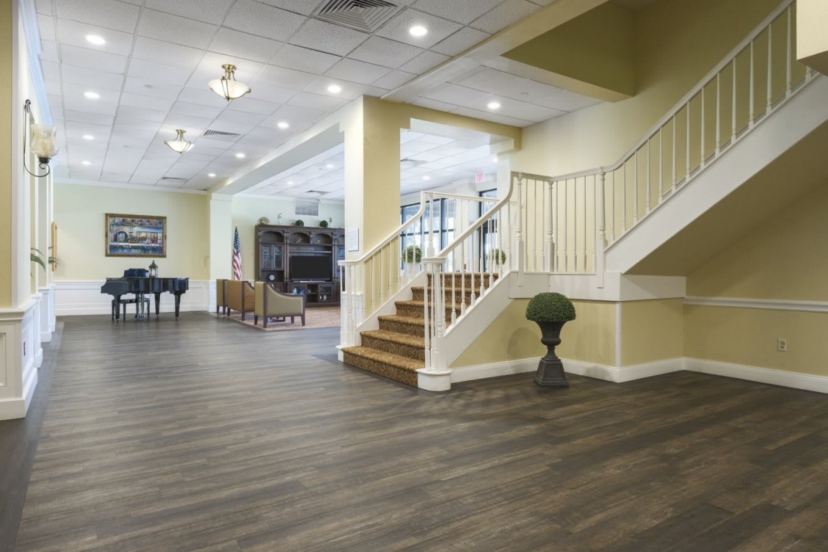 A spacious living area with wood flooring, featuring a staircase, piano, and comfortable seating.