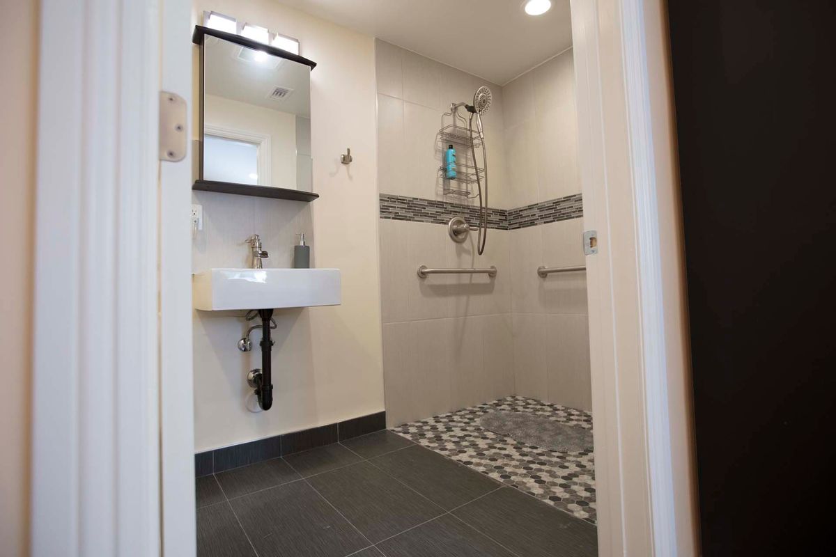 A modern bathroom featuring a wall-mounted sink, mirror, and an open shower area with stylish tile flooring.