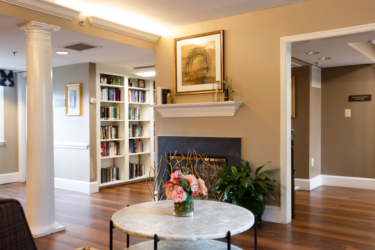 A cozy living room with a bookshelf, a fireplace, and a coffee table adorned with flowers.