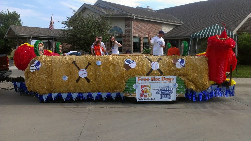 A community parade float with people standing on it, decorated with hay and blue pennants.