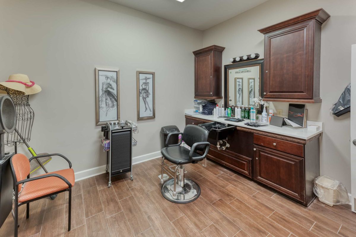 An empty salon room with a styling chair, mirror, and wooden cabinets.