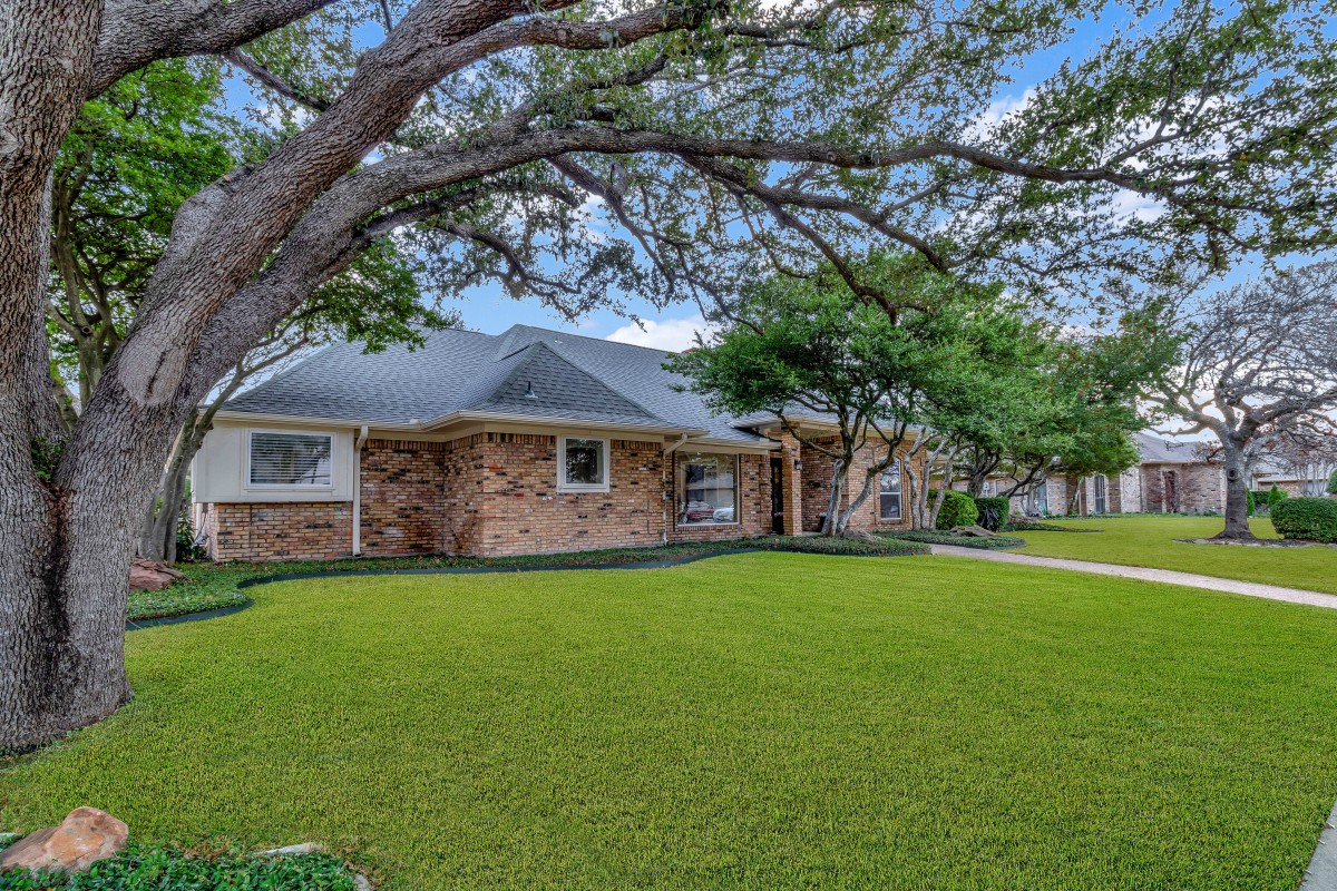 A suburban brick house with a well-maintained lawn and trees.