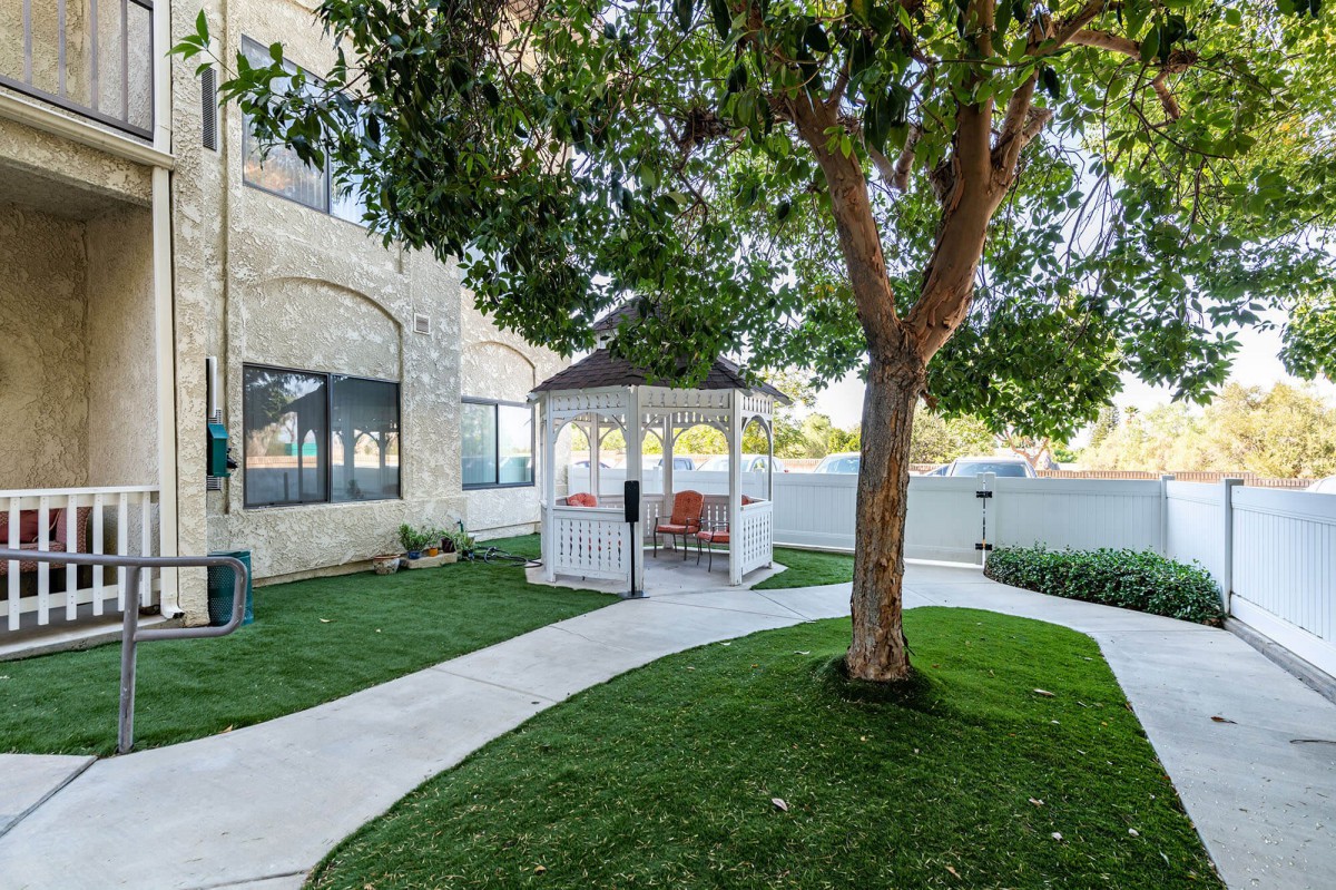 A serene garden with a gazebo, tree, and winding pathway beside a house.