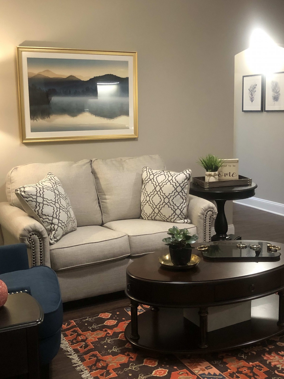 A cozy living room with a sofa, decorative cushions, and a framed landscape painting on the wall.