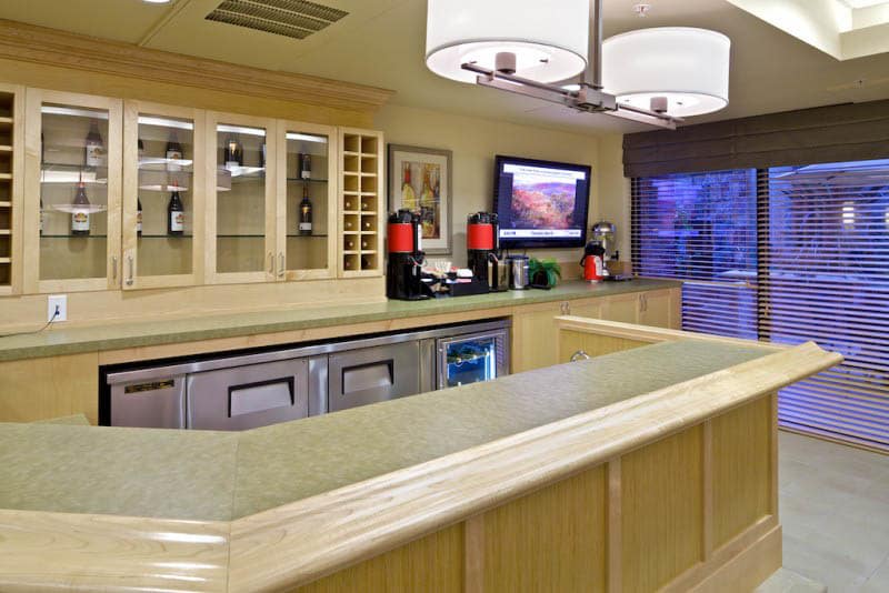 A cozy kitchen and bar area featuring a countertop, cabinets, a coffee station, and a wall-mounted television.