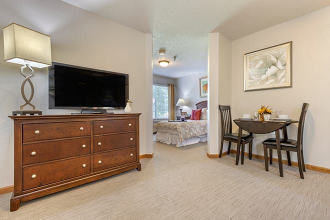 A cozy living space featuring a dresser with a television, leading into a bedroom with a bed and window.