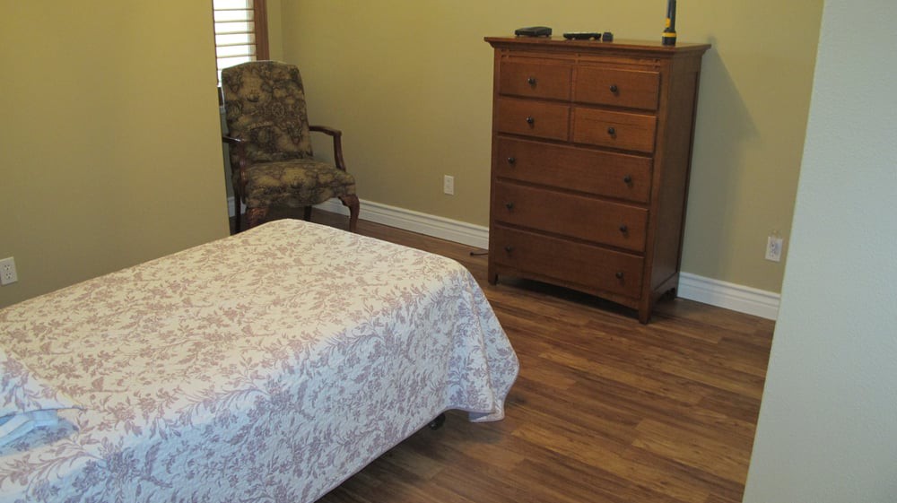 A cozy bedroom with a bed, armchair, and wooden dresser on a hardwood floor.