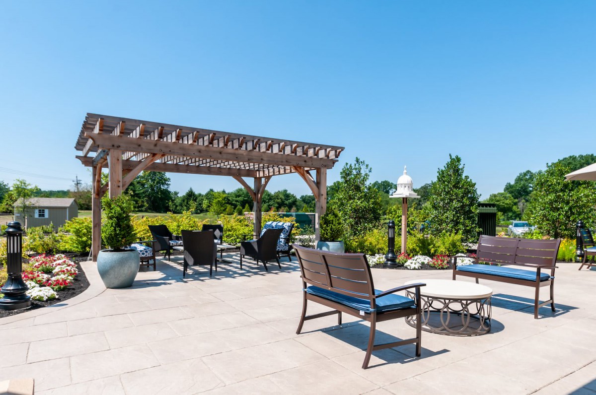 A spacious outdoor patio with a pergola and seating area, surrounded by lush greenery.