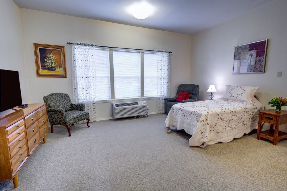 Spacious bedroom with a bed, chairs, and natural light from large windows.