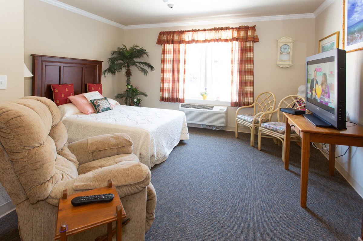 A cozy hotel room with a bed, chairs, and natural lighting from the window.