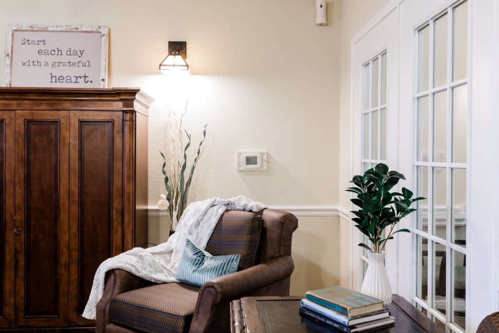 A cozy living room corner with an armchair and a blanket, surrounded by warm lighting and decorative elements.