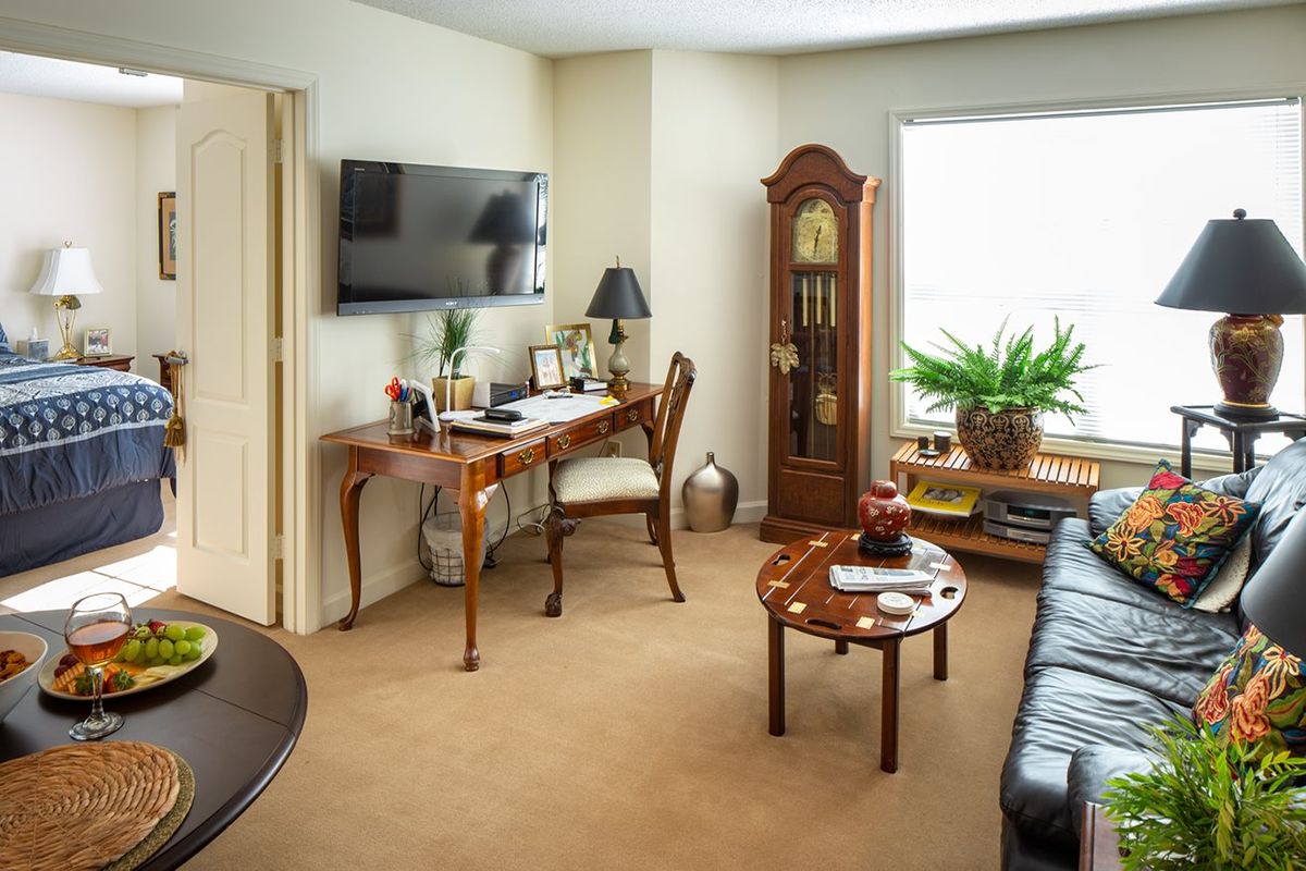 A cozy living room with a desk, grandfather clock, and leather sofa.