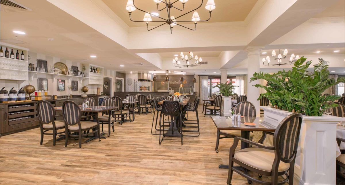 A cozy restaurant interior with wooden floors, stylish chandeliers, and neatly arranged tables and chairs.