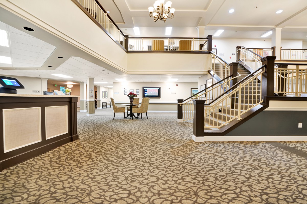 A spacious and elegantly decorated lobby with a carpeted floor, chandelier, and staircase.