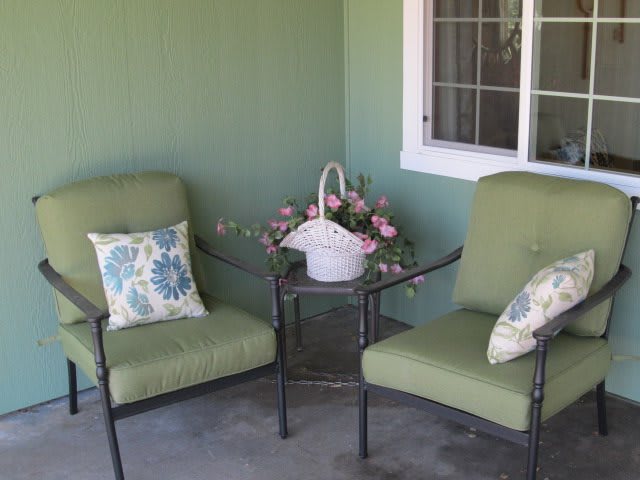 A cozy patio setup with two green cushioned chairs and a small table adorned with a basket of flowers.