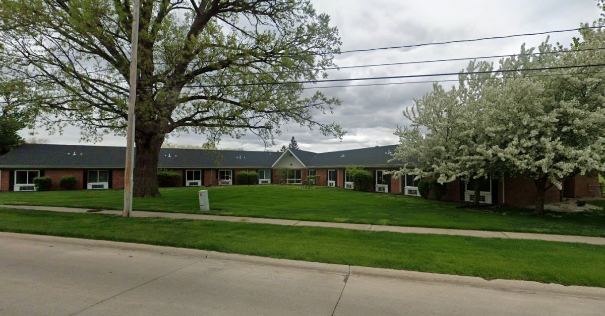 A suburban building surrounded by trees and a well-maintained lawn on a cloudy day.