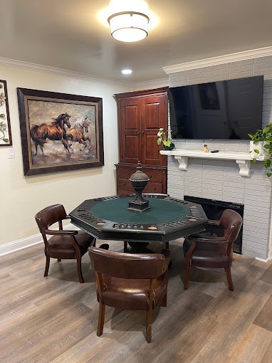 A cozy room featuring a poker table with chairs, a wall-mounted TV above the fireplace, and artwork on the wall.