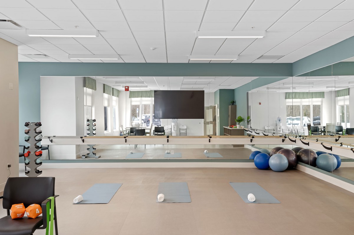 A serene and well-lit yoga studio equipped with mats, therapy balls, and mirrors.