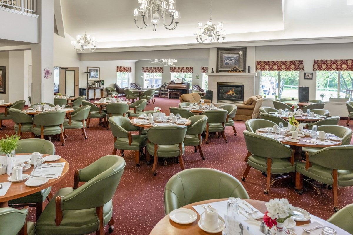A spacious dining area with multiple tables and chairs, featuring elegant chandeliers and a cozy fireplace.