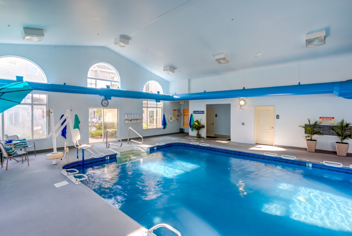 A well-lit indoor swimming pool area with large windows and clean, blue water.