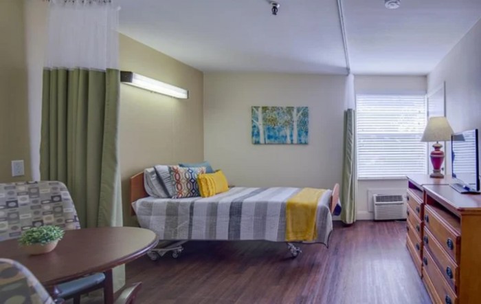 A well-lit hospital room with a neatly made bed, curtains, and a window.