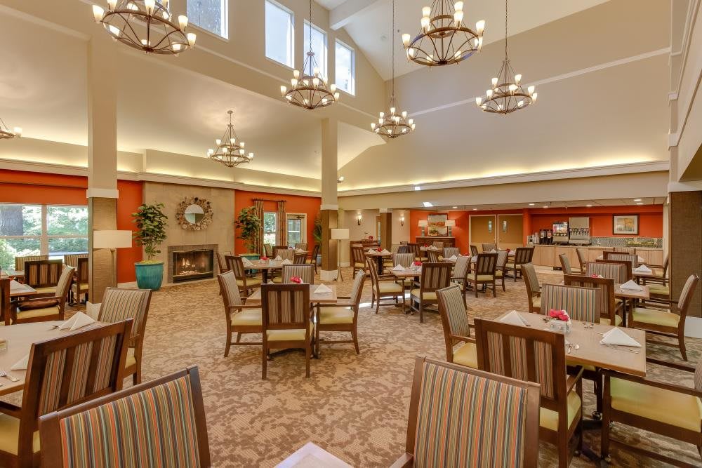 A spacious dining area with elegant chandeliers, well-arranged tables and chairs, providing a warm and inviting atmosphere.