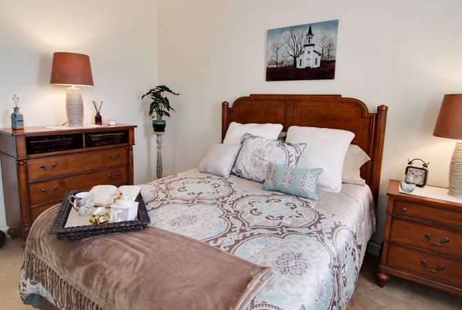 A cozy bedroom with a neatly made bed, decorative pillows, and a nightstand with a lamp.