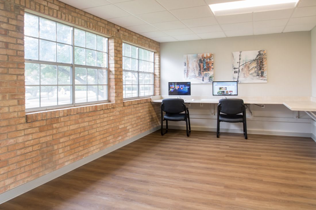 A modern office space featuring a desk with computers, chairs, and large windows that allow natural light to brighten the room.