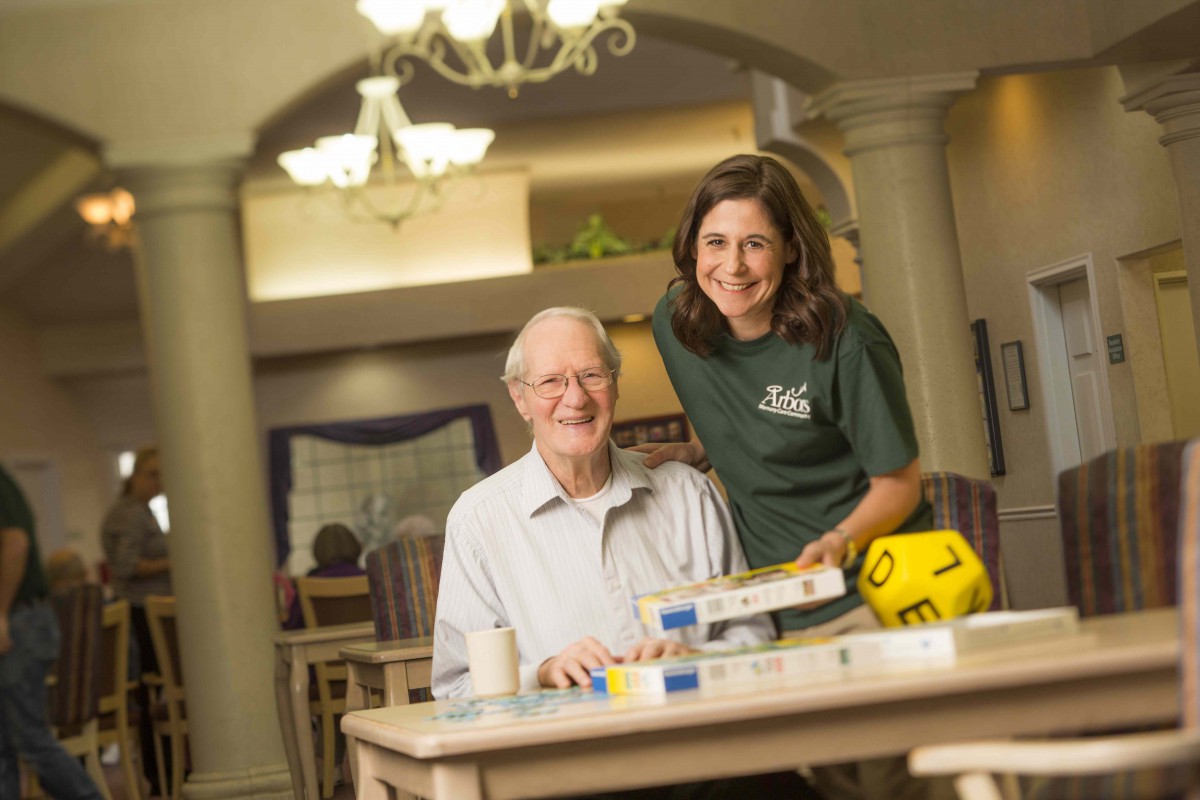 A young woman assisting an elderly man with a board game in a care facility.
