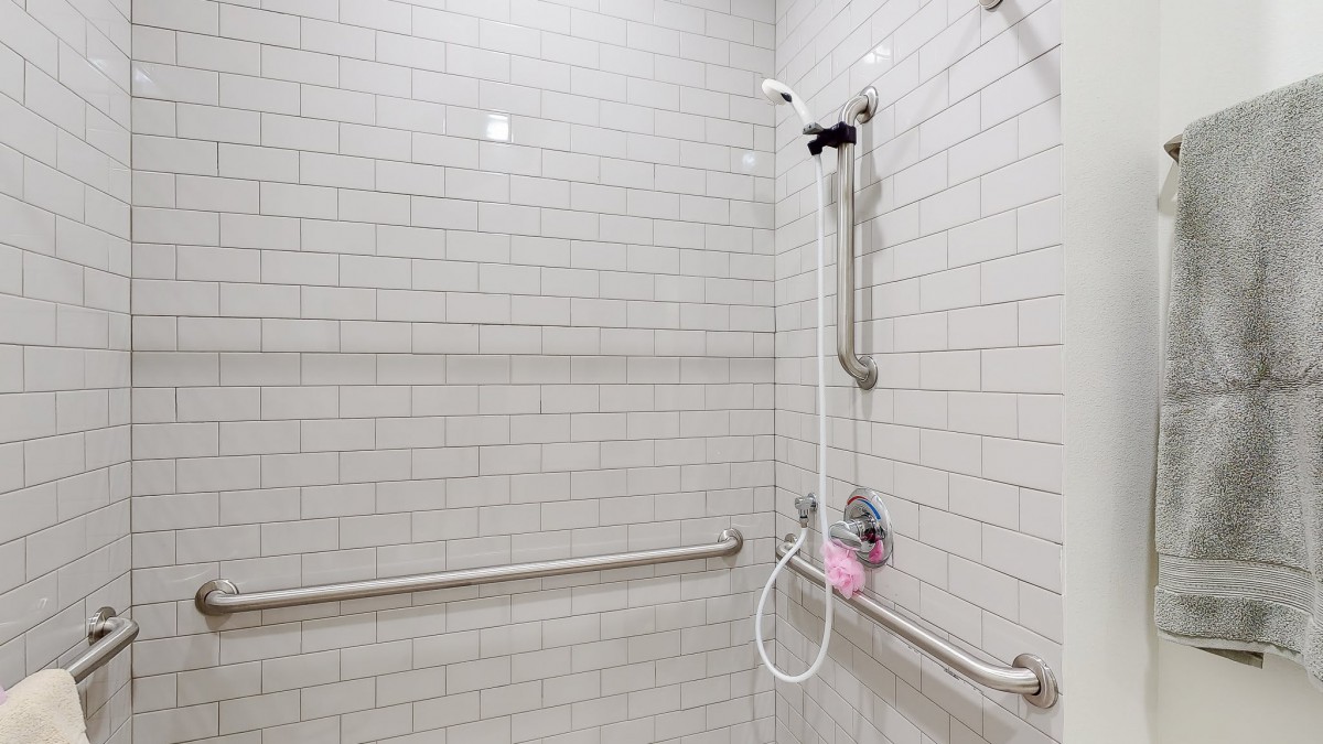 An accessible bathroom shower with white tiles, grab bars, and a handheld showerhead.