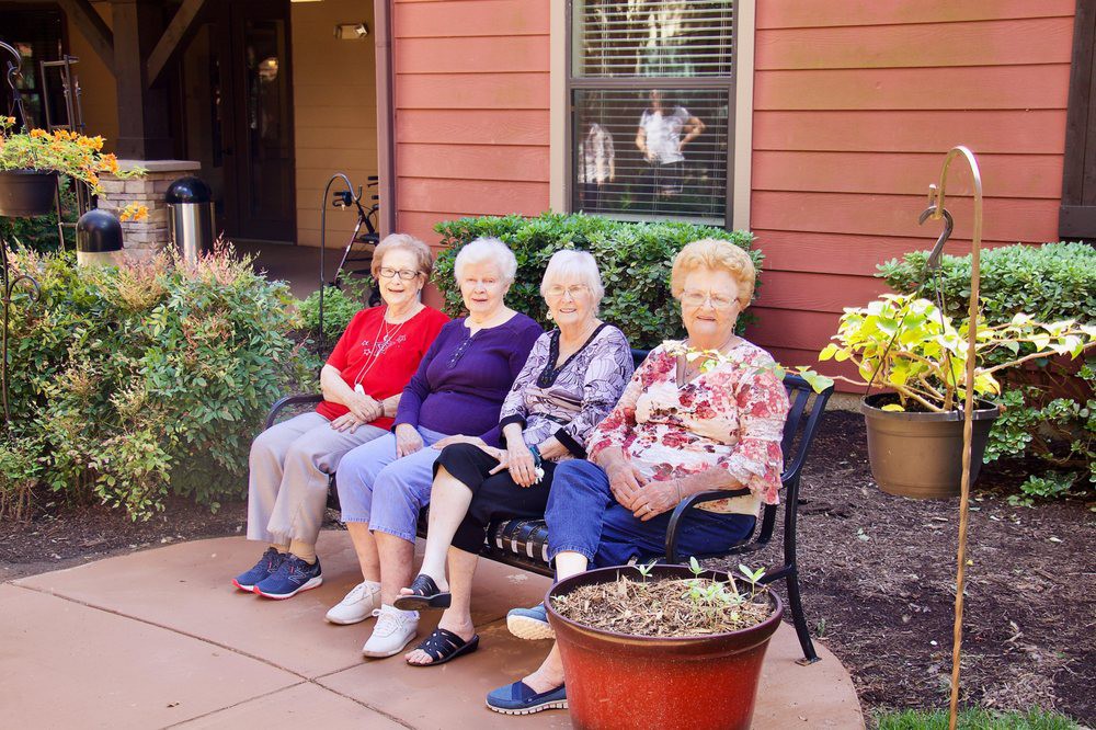 A group of elderly women sitting on a bench in an outdoor garden setting.
