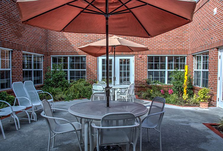 A cozy outdoor patio with tables, chairs, and umbrellas set against a brick building.