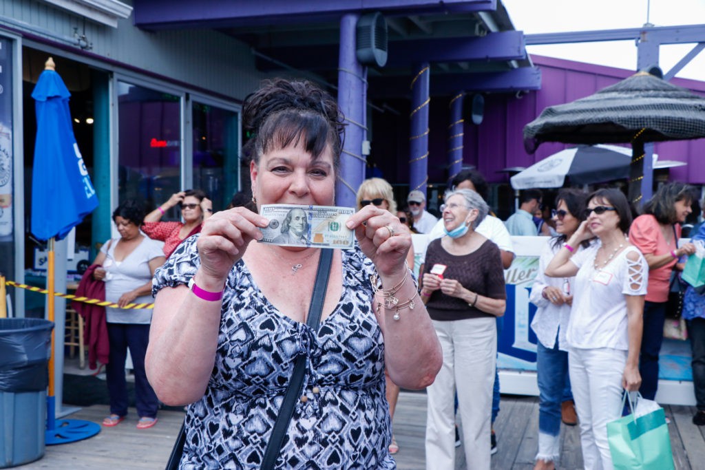 A woman holding a banknote with a group of people in the background during an outdoor event.