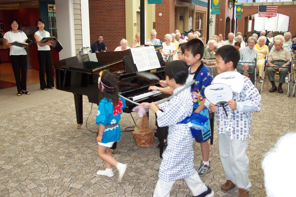 Children in kimonos playing near a piano at an outdoor festival.