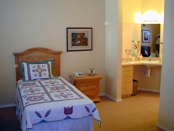 A cozy bedroom with a single bed, decorative quilt, and an adjacent sink area.