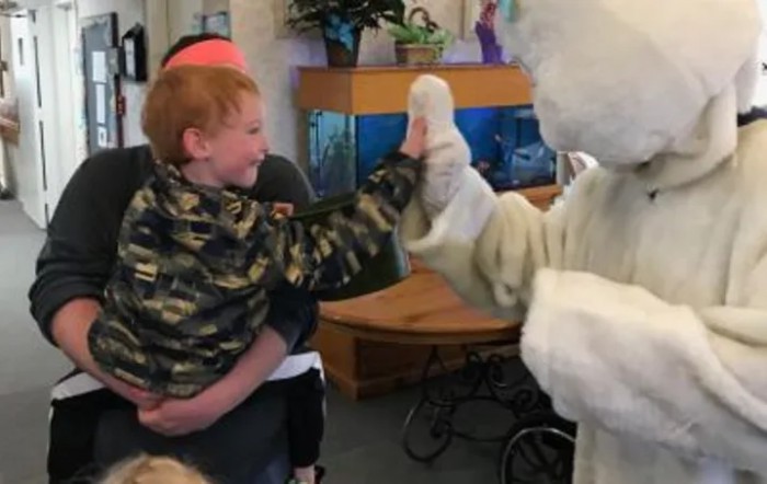 A child gives a high five to a person in a bunny costume at an indoor event.